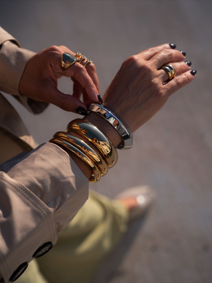 Stacked silver-chrome and gold bangles over a deep plum manicure, catching hard sunlight