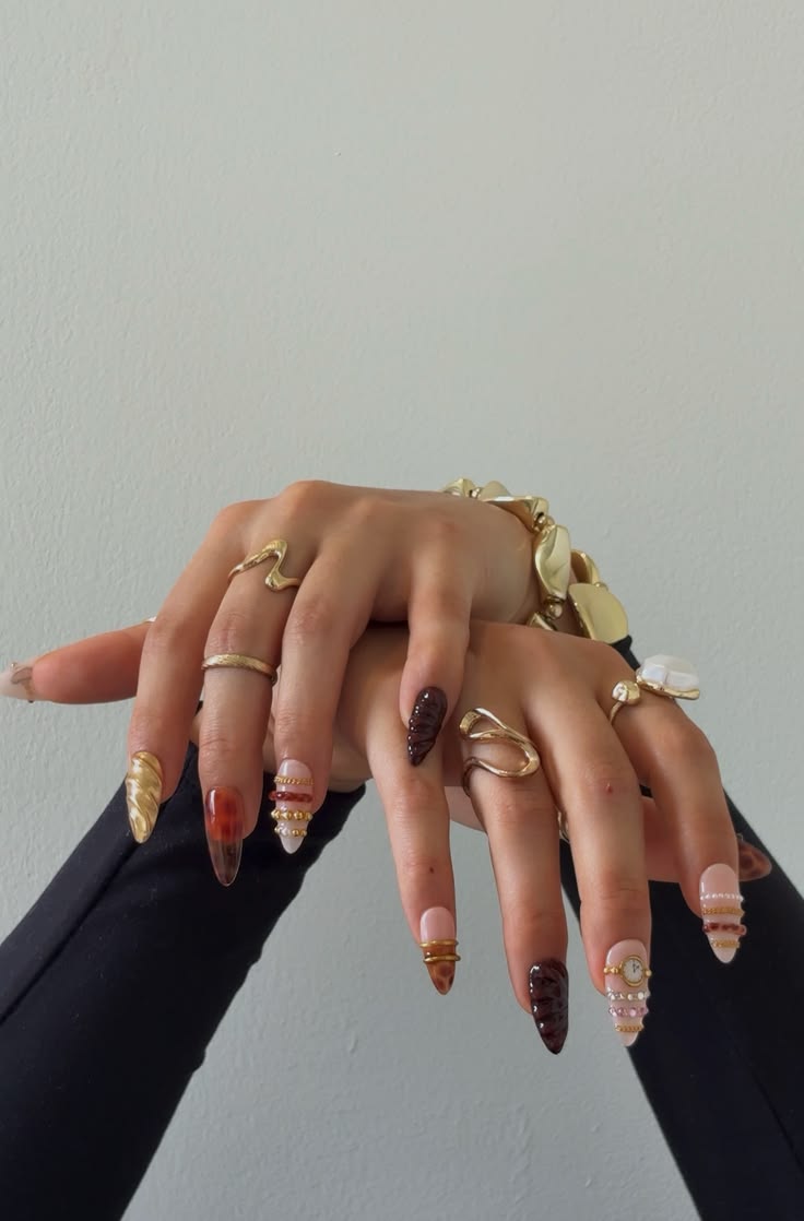 Tortoiseshell and gold chrome press-on nails styled with sculptural gold rings and a chunky bracelet against a soft grey wall