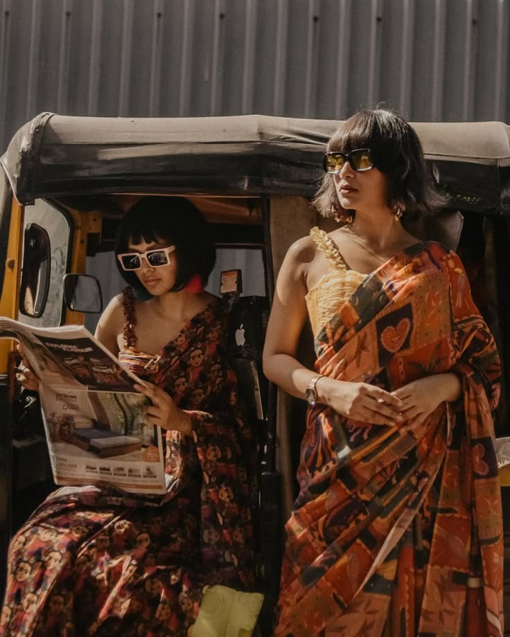 Two women in floral-print sarees and sunglasses beside an auto rickshaw. The street-editorial mood behind our hand-painted floral nail art
